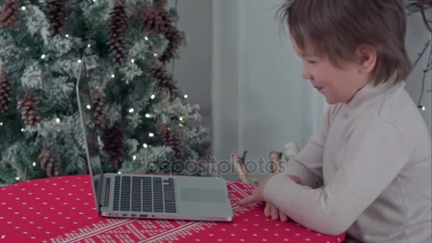 Boy using his laptop sitting at the table near the Christmas tree — Stock Video