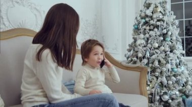Küçük çocuk hediye açıklayan telefonda konuşurken o kanepede oturan annesi ile Noel hediyesi
