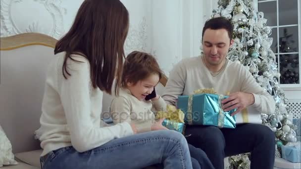 Zoontje praten aan de telefoon, terwijl papa verrassend zijn zoon en vrouw met kerstcadeaus — Stockvideo