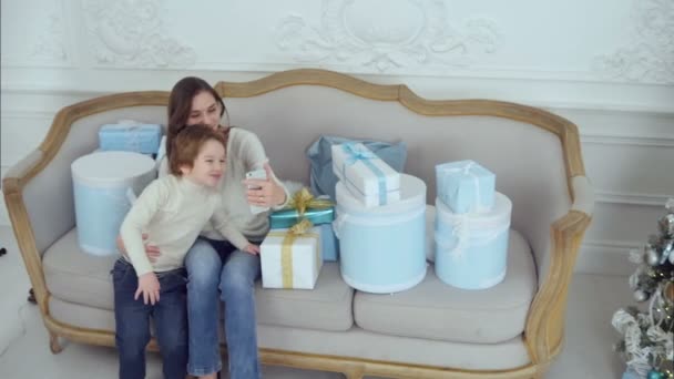 Jovem mãe e filho feliz cercado por presentes de Natal tirando selfies com telefone — Vídeo de Stock