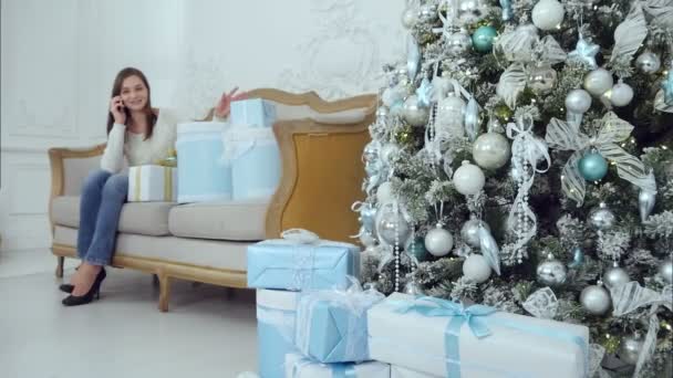 Glückliche Mutter telefoniert, während ihr kleiner Sohn Weihnachtsgeschenke auf dem Sofa bringt — Stockvideo