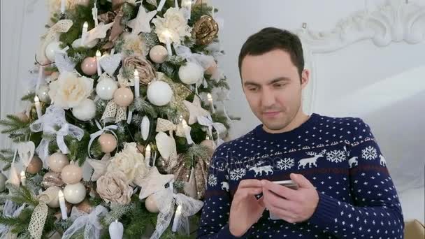 Jovem feliz em malhas de Natal enviando mensagens através de seu telefone — Vídeo de Stock