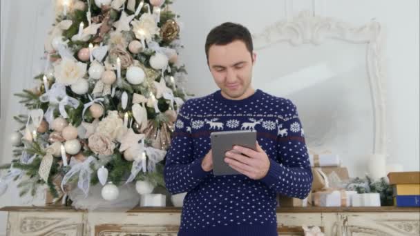Молодий чоловік у різдвяному трикотажі перевіряє планшет — стокове відео