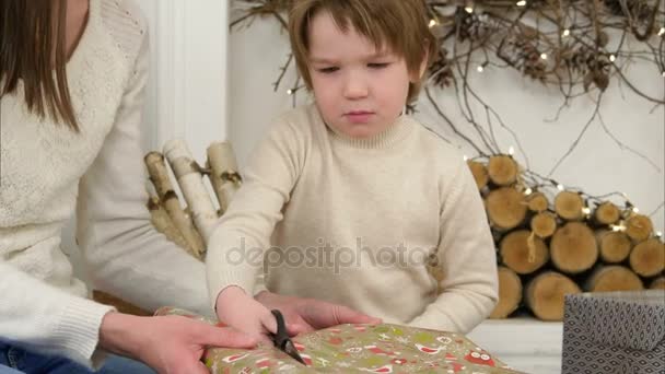 Niño serio ayudando a su madre a cortar papel de regalo de Navidad — Vídeos de Stock