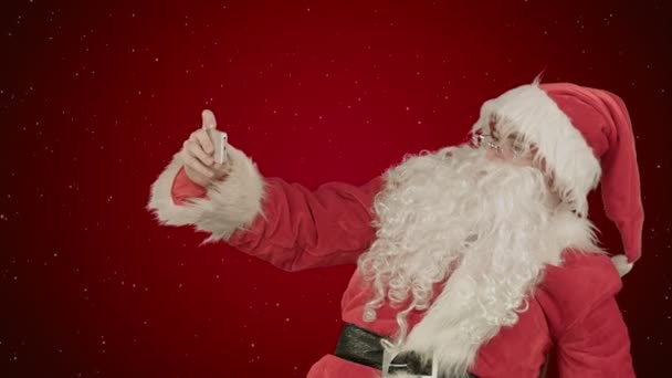 Kerstman maken selfie, houden een grote cadeau op rode achtergrond met sneeuw — Stockvideo