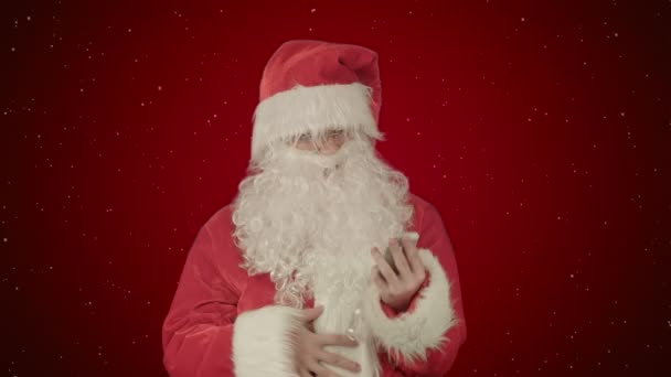 Santa claus να διαβάζει και να στέλνει μηνύματα κειμένου από το τηλέφωνο κυττάρων σε κόκκινο φόντο με χιόνι — Αρχείο Βίντεο