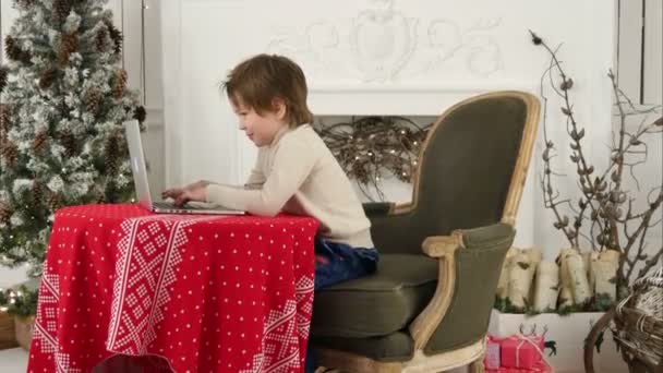 크리스마스 트리 근처 노트북에 산타 클로스에 게 편지를 입력 하는 어린 소년 미소 — 비디오