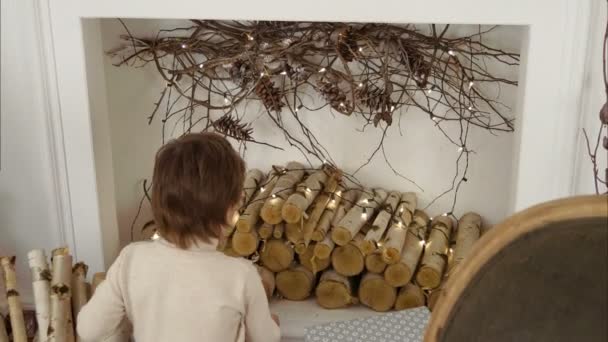 Kleiner Junge legt Baumstämme in weihnachtlich dekorierten Kamin — Stockvideo