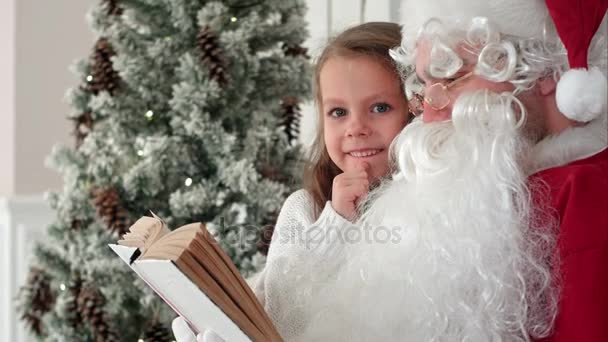 Santa Claus könyvet olvasva, aranyos lány, a karácsonyfa közelében — Stock videók