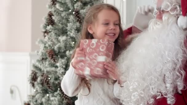 Szczęśliwa dziewczynka uśmiechający się starając się odgadnąć, co jest w środku jej świąteczny prezent od Mikołaja — Wideo stockowe