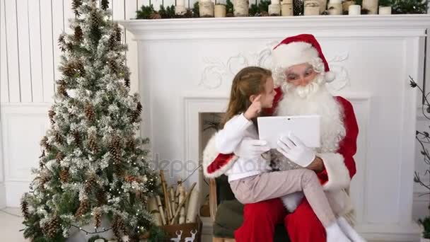 Menina feliz e Papai Noel olhando presentes no PC tablet ao lado da árvore de Natal — Vídeo de Stock