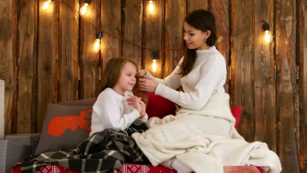 Junge Mutter im weißen Pullover, die ihrer Tochter die Haare flechtet — Stockvideo