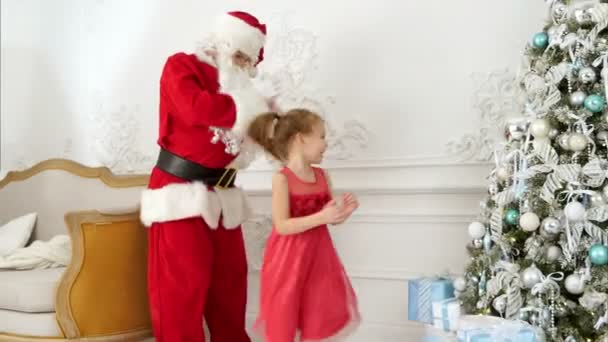 Санта-Клаус хлопает в ладоши, когда вокруг него танцует красивая маленькая девочка. — стоковое видео