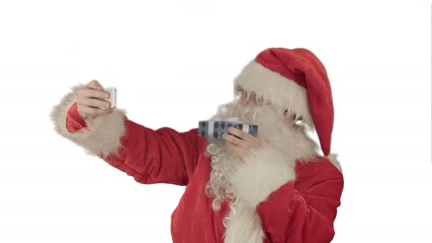 Santa Claus sosteniendo un gran regalo haciendo una selfie en el teléfono inteligente sobre fondo blanco — Vídeos de Stock