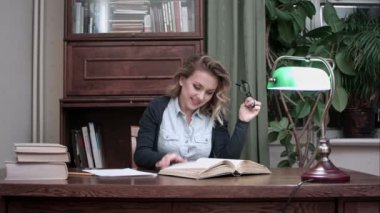 Masasında oturan ve mutlu bir şekilde bir kitap aracılığıyla gidiş gülümseyen kadın