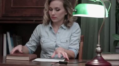 Genç kadın bir kitap ile masaya oturur, yeşil lamba yanar ve çalışmaya başlar