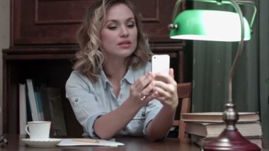 Kitaplar ile masada oturan ve komik selfies ile telefonunu alarak rahat youn kadın