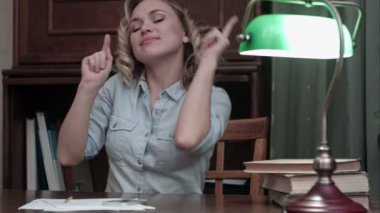 Kitaplarla masasında oturan ve komik biraz dans olan genç ve güzel kadın