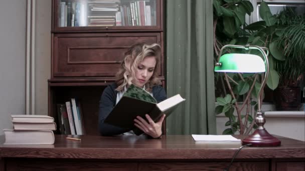 Hübsche junge Frau sitzt an ihrem Schreibtisch und recherchiert Informationen im Buch für Geschäftsbericht — Stockvideo