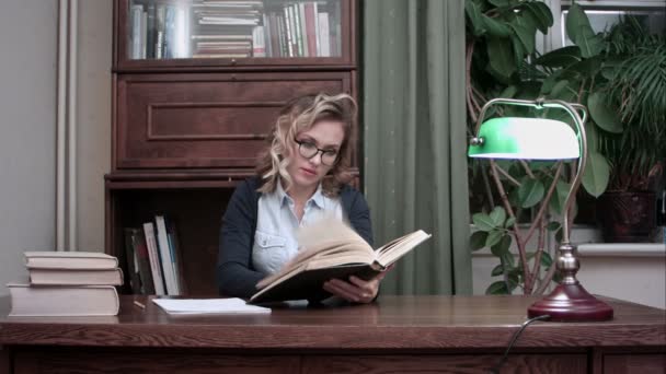 彼女の研究室でテーブルに座って本を探るメガネの若い女性に焦点を当てた — ストック動画