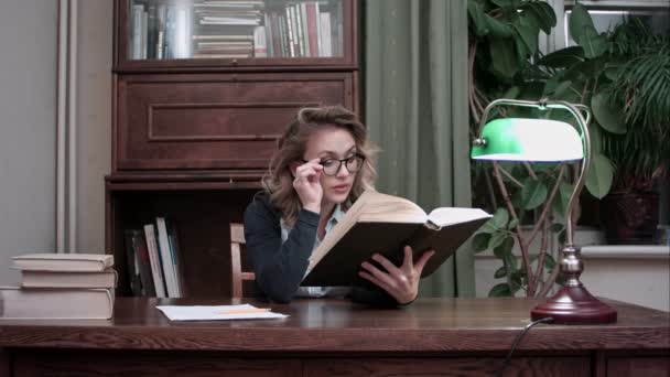 Mladá inteligentní žena v brýlích drží knihu a nadšeně čtení — Stock video