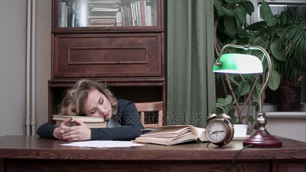 Mujer cansada tomando una siesta en un montón de libros en su lugar de trabajo y siendo despertada por una alarma — Vídeos de Stock