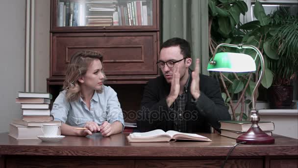 Dos jóvenes científicos teniendo una lluvia de ideas sentados a la mesa con un libro abierto — Vídeos de Stock