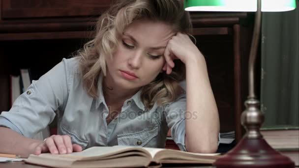 Mujer joven y cansada durmiendo sobre un libro mientras está sentada a la mesa después de un largo día de trabajo — Vídeos de Stock