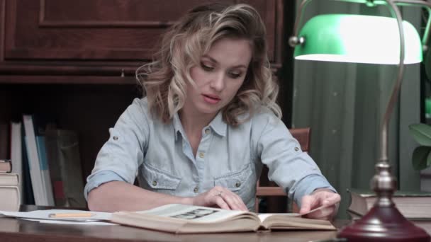 Giovane donna studiando attentamente il libro sulla sua scrivania — Video Stock