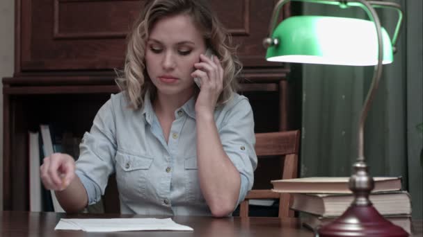Müde junge Frau sitzt am Schreibtisch und bekommt schlechte Nachrichten am Telefon — Stockvideo