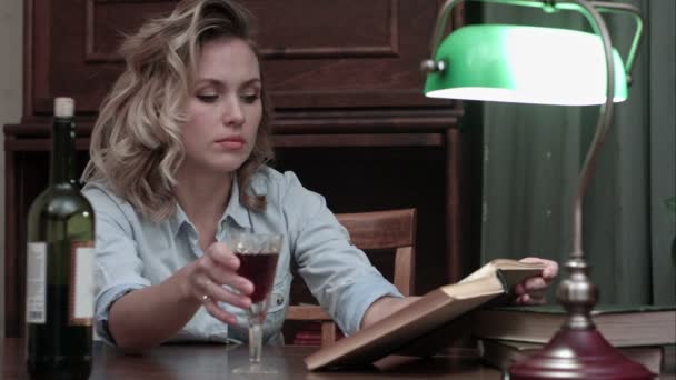 Znudzona kobieta wypija szklankę wina siedzi przy stole i czytanie książek — Wideo stockowe