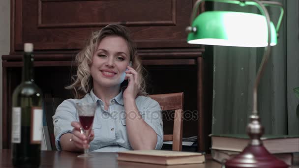 Atrakcyjna, młoda kobieta, kieliszku wina siedzi przy biurku podczas rozmowy telefonicznej po dniu długiej pracy — Wideo stockowe