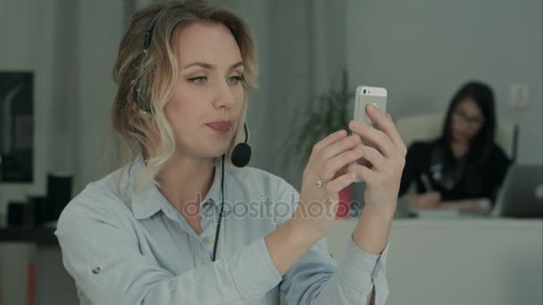 Trabajadora de oficina joven en auriculares tomando selfies en su teléfono — Vídeos de Stock