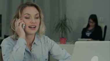 Ofis Masası oturma ve cep telefonuyla konuşurken gülümseyen genç kadın