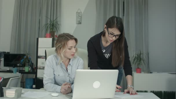 Две женщины-коллеги обмениваются идеями по поводу отчета, глядя на ноутбук — стоковое видео