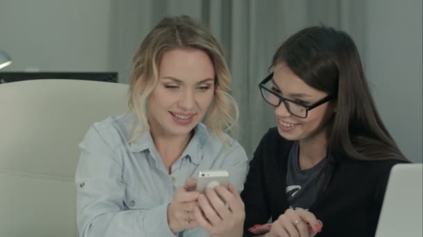 Двое улыбающихся коллег смотрят на свои фотографии по телефону — стоковое видео