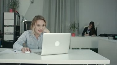 Genç bir kadın işçi ofiste dizüstü üzerinden görüntülü arama yapma