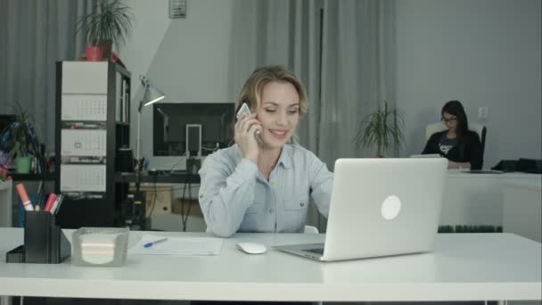 Две сотрудницы, работающие вместе, отвечают на телефонные звонки в офисе — стоковое видео