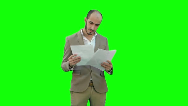 Serious young businessman standing and reading some documents on a Green Screen, Chroma Key. — Stock Video