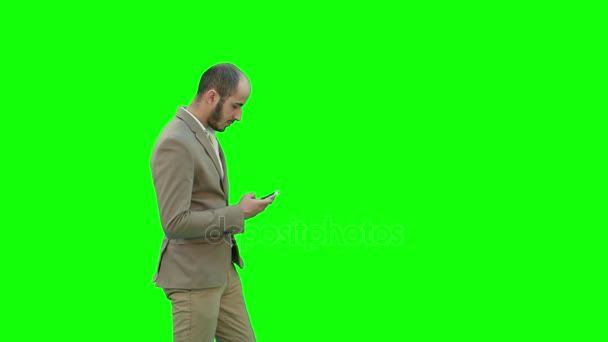 Junger Mann im Anzug geht und sendet SMS auf Handy auf grünem Bildschirm, Chroma-Schlüssel. — Stockvideo