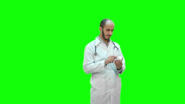 Médico masculino leyendo atentamente la etiqueta del medicamento de un frasco de pastillas en una pantalla verde, Chroma Key . — Vídeo de stock