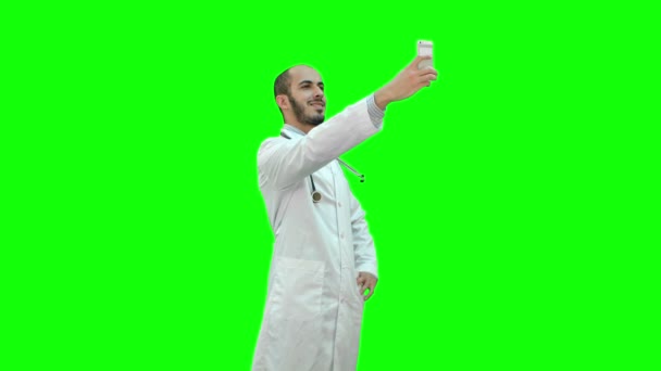 Usmívající se doktor v bílém plášti s stetoskop, přičemž selfie na svém telefonu na zelené obrazovce, Chroma Key. — Stock video