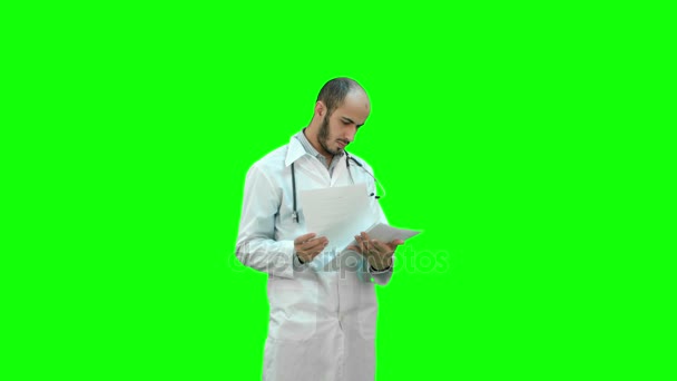 Αρσενική ιατρική γιατρός ελέγχοντας τα χαρτιά του σχετικά με μια πράσινη οθόνη, Chroma Key. — Αρχείο Βίντεο