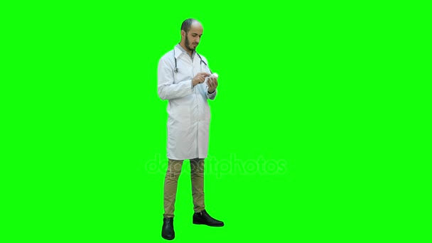 Médico masculino leyendo atentamente la etiqueta en una botella de pastillas en una pantalla verde, Chroma Key . — Vídeo de stock