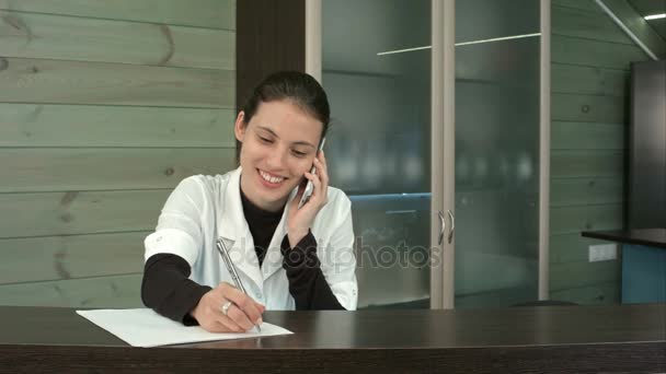 Smiling spa receptionist talking to client over the phone and filling in form