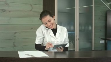 Resepsiyon masasında tablet ve not almak kullanırken telefonda konuşurken gülümseyen güzellik salonu Yöneticisi