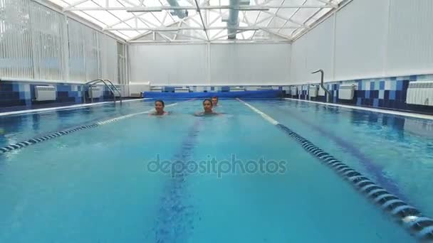 Dos mujeres jóvenes nadando en la piscina con un hombre joven nadando detrás de ellas — Vídeo de stock