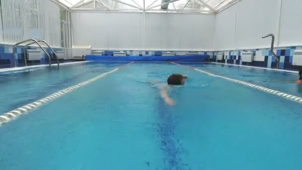 Två leende unga kvinnor simning i olika pool gränderna med en ung man simma crawl i mitten körfält — Stockvideo