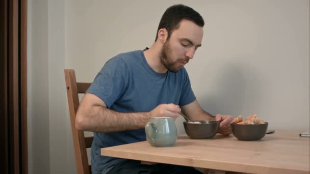 Молодой человек на завтрак ест кашу и круассаны — стоковое видео