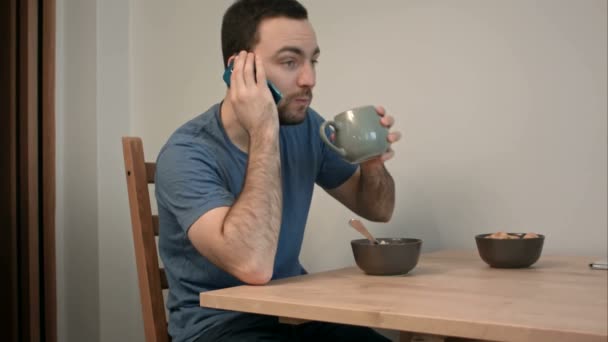 Молодой человек разговаривает по телефону за завтраком — стоковое видео